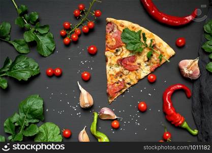 triangular slice of baked pizza with mushrooms, smoked sausages, tomatoes and cheese, next to fresh green leaves of arugula, black background, flat lay