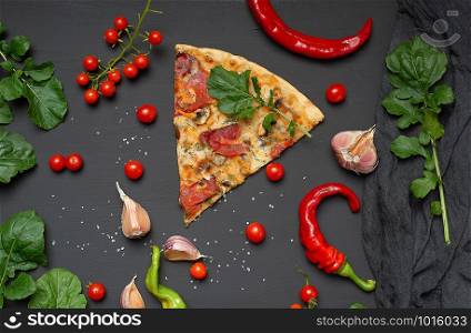 triangular slice of baked pizza with mushrooms, smoked sausages, tomatoes and cheese, next to fresh green leaves of arugula, black background, flat lay