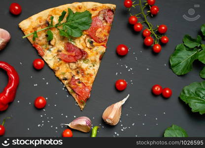 triangular slice of baked pizza with mushrooms, smoked sausages, tomatoes and cheese, next to fresh green leaves of arugula, black background, flat lay