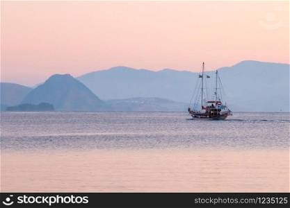 Trip boat leaving the harbour and sailing off into the distance at dawn, Kos, Greece