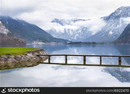 Trip idea theme image with the Hallstatter lake, a small bridge that crosses it and the majestic Northern Limestone Alps, located in Hallstatt town, Austria.