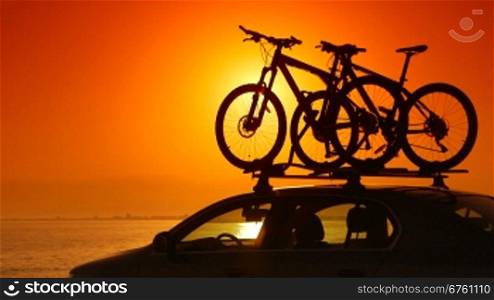 Trip on summer beach by car with mounted bikes at sunset