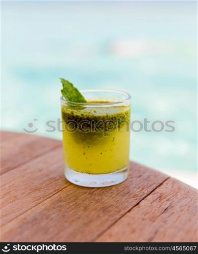 trivet, tourism, drinks and food concept - glass of fresh juice or cocktail on table at beach