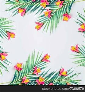 Tropical background with palm leaves and exotic flowers on white background, top view. Frame. Flat lay. Copy space for your design