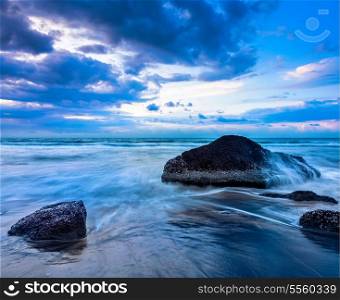 Tropical beach vacation background - waves and rocks on beach on sunset with beautiful cloudscape