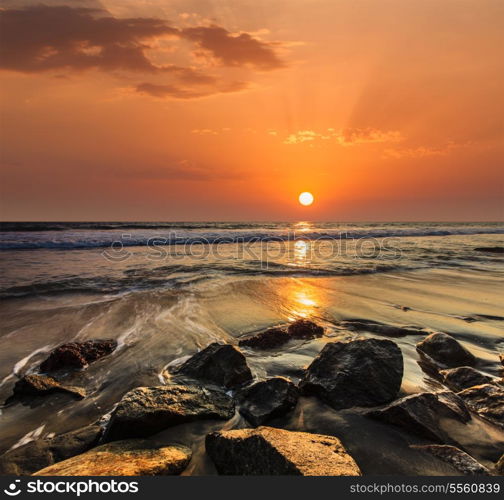 Tropical beach vacation background - waves and rocks on beach on sunset with beautiful cloudscape