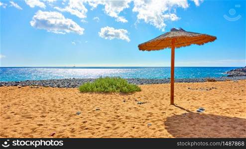 Tropical beach with straw parasol by the sea on sunny summer day