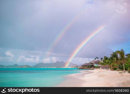 Tropical beach with turquoise water in the ocean, white sand and colorful rainbow over the sea. Beach sunbed on exotic tropical resort on caribs