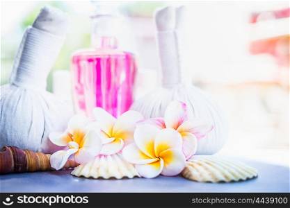 Tropical Frangipani flowers with herbal compress stamps , pink lotion bottle and shells at nature background. Spa or wellness background