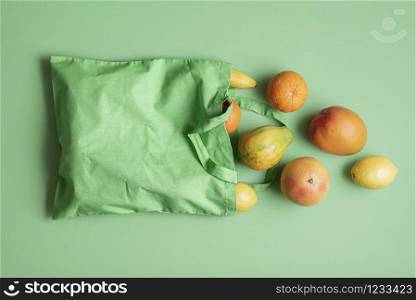 Tropical fruits in a green fabric bag on a green background. Exotic summer fruits in a reusable bag. Fresh fruit sale. Food shopping concept.
