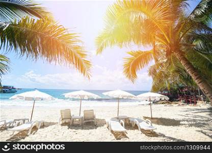 Tropical Holiday coconut leaf palm tree on the beach with sun light on blue sky sea and ocean background / Summer vacation nature travel beautiful summer landscape with chair beach umbrella on sand