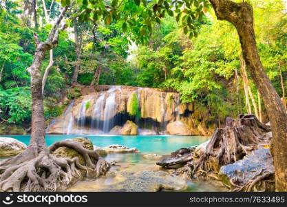 Tropical landscape with beautiful waterfall, emerald lake, rocks and large tree roots in wild jungle forest. Erawan National park, Kanchanaburi, Thailand