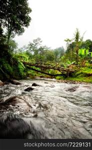 Tropical landscape with rocky river under the wooden bridge and typical rural Indonesian house in the Jungle of west Java
