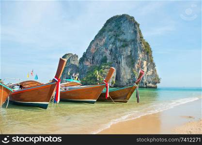 Tropical landscape with row of traditional thailand longtail boats at sand beach with clear water and rock island on background