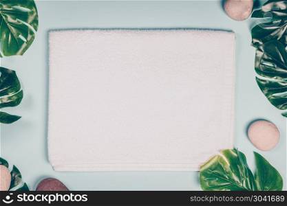 Tropical leaves Monstera, white towel and stones on blue background. Flat lay, top view. Tropical leaves Monstera, white towel and stones