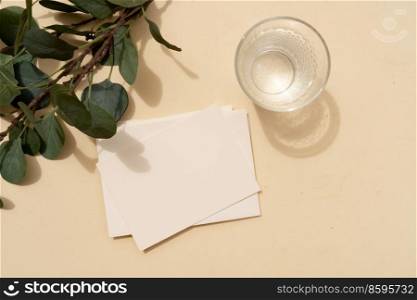 Tropical summer stationery mock-up scene. Blank business card, green eucaliptus leaves, glass of water on beige textured table background. Flat lay, top view. summer stationery mock-up scene.