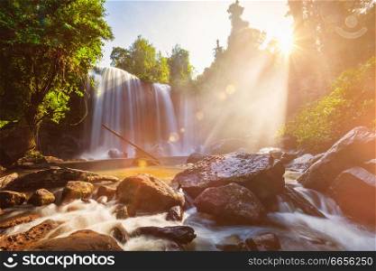 Tropical waterfall in the morning with sun rays in Cambodia. Lens flare and light leak. Tropical waterfall in the morning