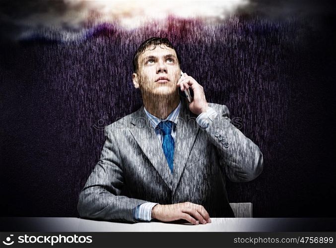 Troubles in business. Young troubled businessman sitting under rain and talking on phone
