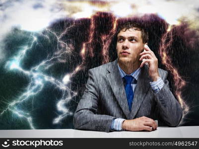 Troubles in business. Young troubled businessman sitting under rain and talking on phone