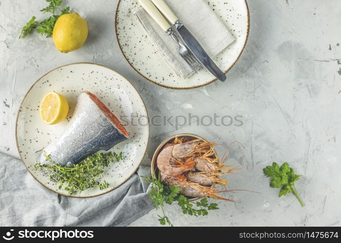 Trout fish surrounded parsley, lemon, shrimp, prawn in ceramic plate. Light gray concrete table surface. Healthy seafood background.
