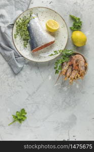 Trout fish surrounded parsley, lemon, shrimp, prawn in ceramic plate. Light gray concrete table surface. Healthy seafood background.