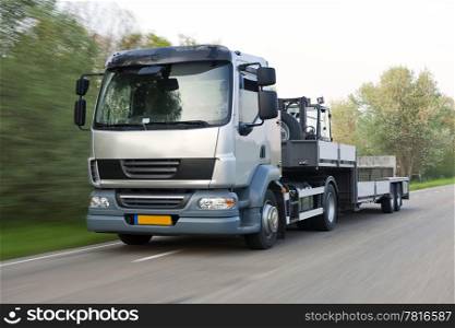 Truck and trailer combination, carrying a forklift, driving at speed