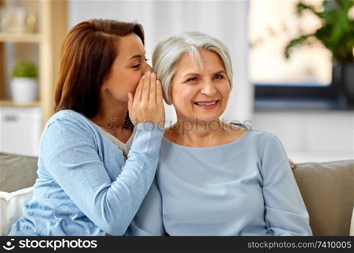 trust, gossiping and family concept - adult daughter whispering secret to senior mother at home. adult daughter whispering to senior mother at home