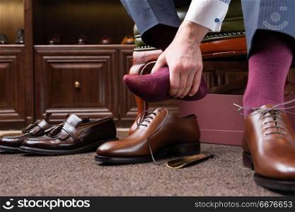 Trying new tight shoes. Man is putting on a new pair of luxury brown full grain leather shoes at footwear store and holding foot painfully. Old shoes left behind.. men shoes boutique store