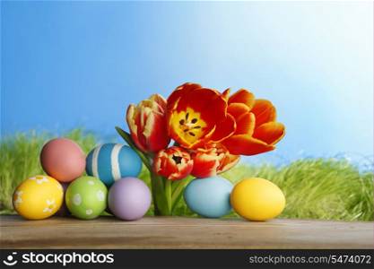 Tulips and easter eggs over green grass and blue sky background