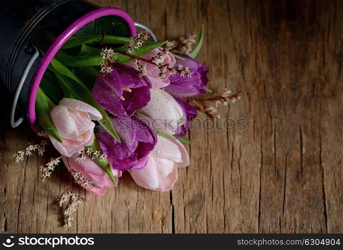 Tulips with drops in a bucket on a wooden table