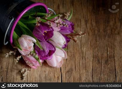 Tulips with drops in a bucket on a wooden table