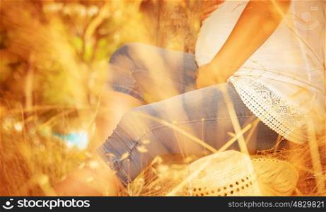 Tummy of expectant woman, body part, female expecting for a baby, sitting down on dry grass in autumnal park, new life concept