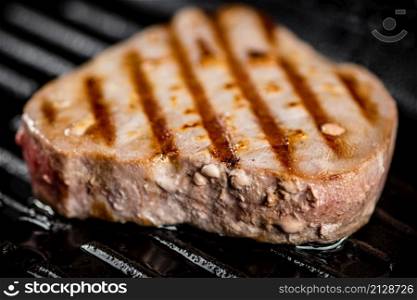Tuna steak in a grill pan. On a black background. High quality photo. Tuna steak in a grill pan.