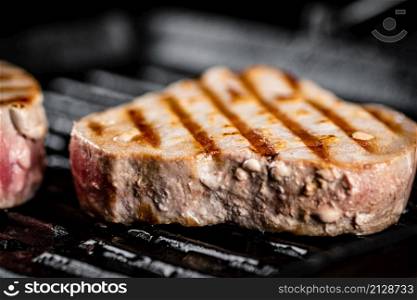 Tuna steak in a grill pan. On a black background. High quality photo. Tuna steak in a grill pan.