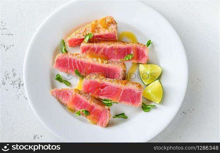 Tuna steak with sesame seeds with herbs and lime wedges