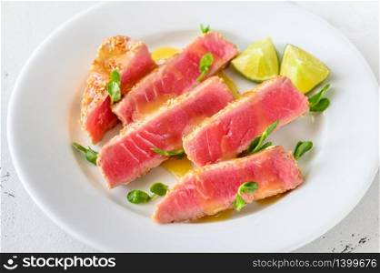 Tuna steak with sesame seeds with herbs and lime wedges
