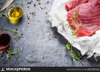 Tuna steaks in wrapping paper with cooking ingredients on dark rustic background, close up. Seafood concept