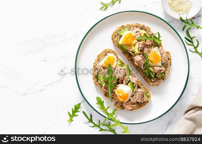 Tuna toast. Open sandwiches with whole grain bread, canned tuna, boiled egg, avocado and arugula. Top view