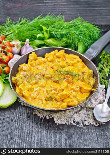 Turkey meat goulash with tomato, zucchini, sour cream and thyme in a pan on burlap napkin, spoon and garlic on wooden board background