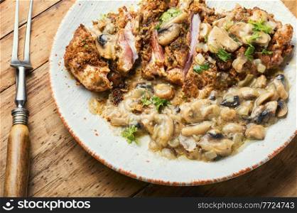 Turkey meat in cheese breading with mushroom sauce on rustic wooden table. Turkey schnitzel with fried mushrooms