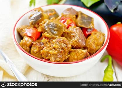 Turkey or pork meat stew with eggplant, onion, tomato and pepper in a bowl, napkin, basil and parsley on white wooden board background