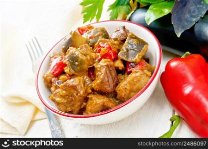 Turkey or pork meat stew with eggplant, onion, tomato and pepper in a bowl, napkin, basil and parsley on wooden board background