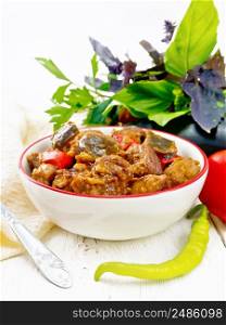 Turkey or pork meat stew with eggplant, onion, tomato and pepper in a bowl, towel, basil and parsley on light wooden board background