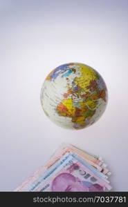 Turkish Lira banknotes by the side of a model globe on white background