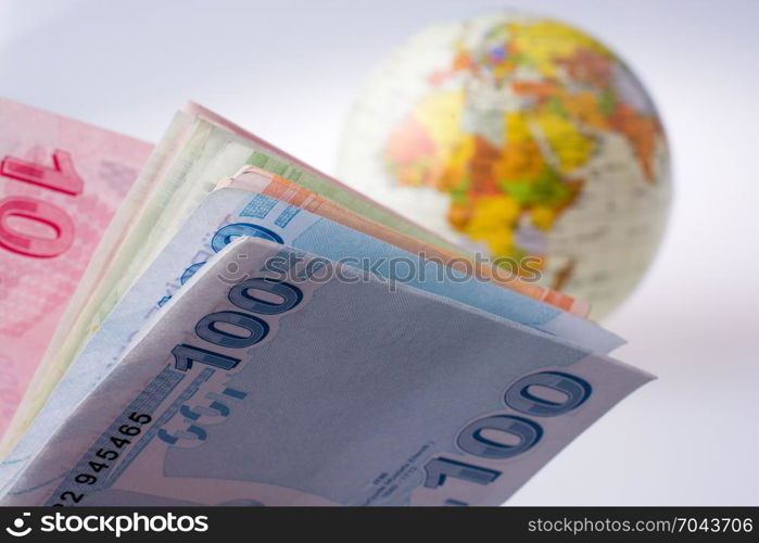 Turkish Lira banknotes by the side of a model globe on white background