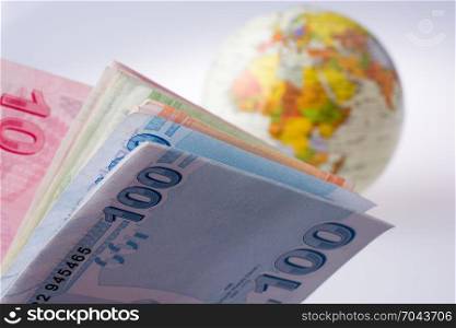 Turkish Lira banknotes by the side of a model globe on white background