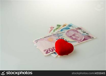 Turkish Lira banknotes by the side of a red color heart shaped object on white background