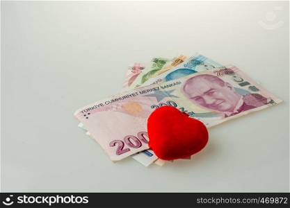 Turkish Lira banknotes by the side of a red color heart shaped object on white background