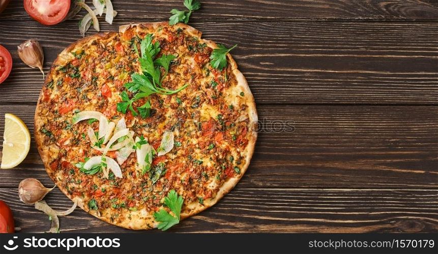 Turkish pizza lahmajun with minced lamb and beef on a thin crust with vegetables and herbs, horizontal layout. Wooden table, top view, flat lay, copy space