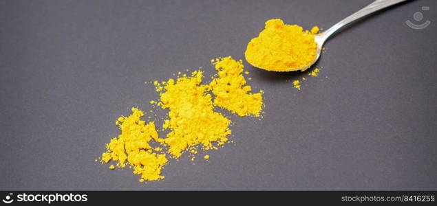 Turmeric or curcuma powder on metal spoon and scattered on dark background.. Turmeric powder on metal spoon